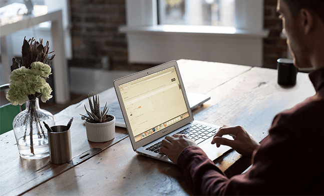 A picture of a young man sitting on a table studing on a laptop, cozy at home